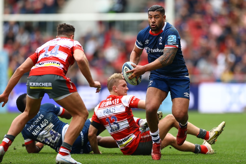 Salesi Piutau runs with the ball as another player prepares to tackle him.