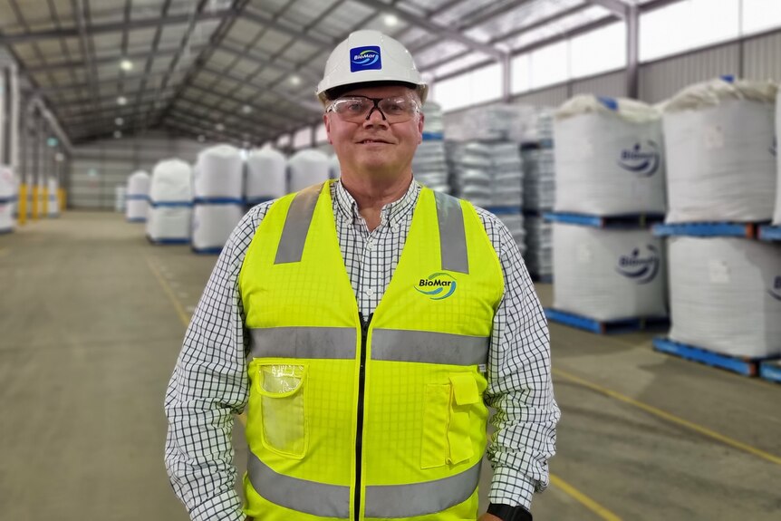 David Whyte stands in a large warehouse with packed white bags on blue pallets behind him