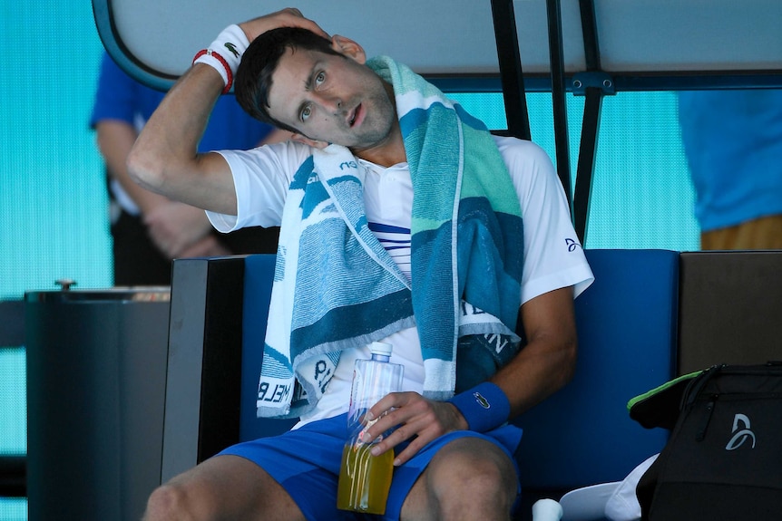 Novak Djokovic tilts and touches his head at a change of ends.