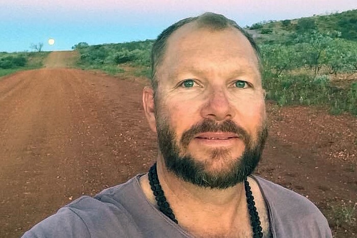 A man looks at the camera with a full moon rising behind him.