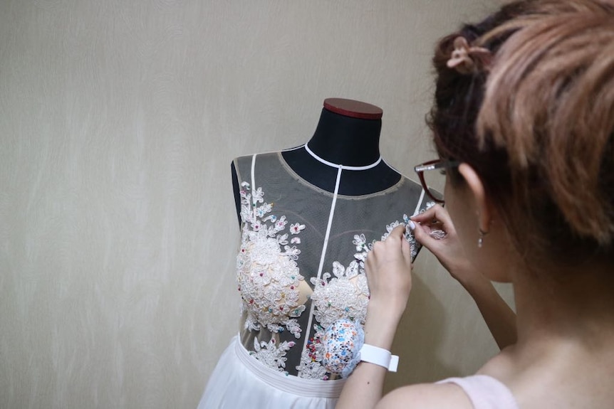 Woman puts beads on a wedding dress.