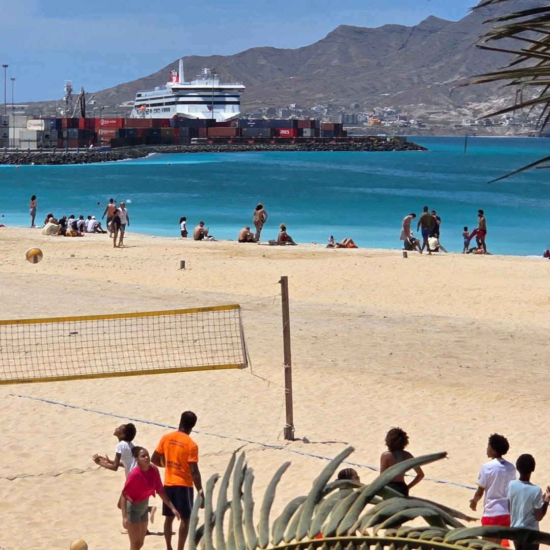 A beach with people, with large ship in background.