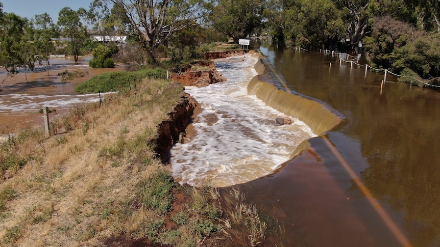 Part of a road collapsed with water gushing through farmlands