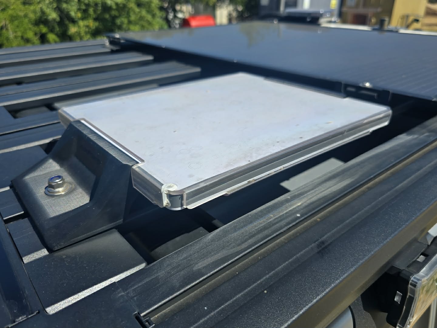 Um objeto plano e quadrado está aparafusado ao teto de um veículo com painel preto. 