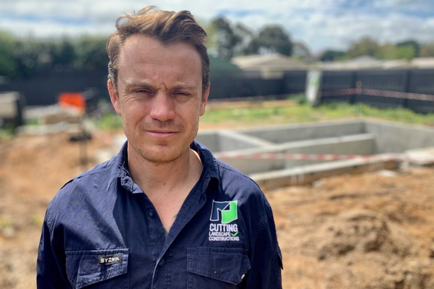 A man stands in front of a back yard under construction.