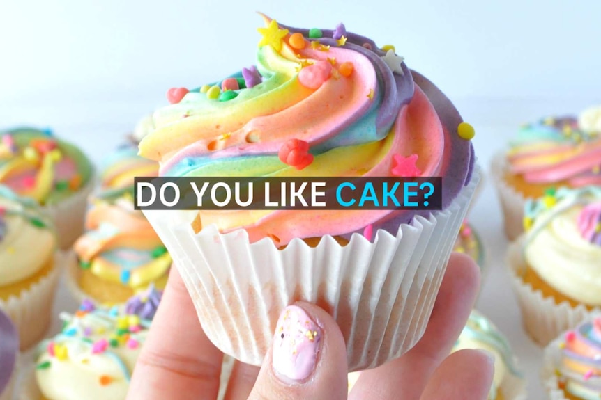 A hand holds a cupcake with rainbow icing and sprinkles