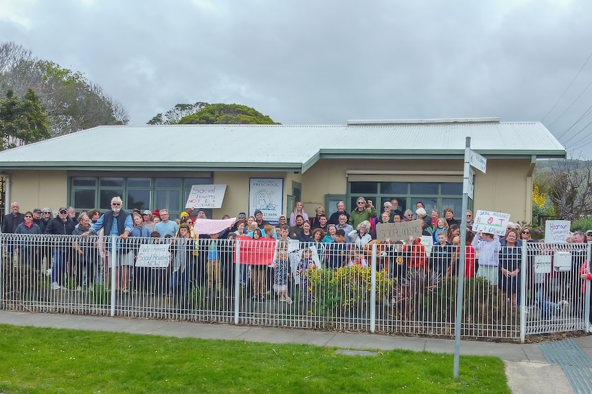 A group of people stand behind a fence in front of a building holding signs 