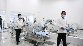 Indonesian president Joko Widodo in a face mask an white coat walks past hospital beds