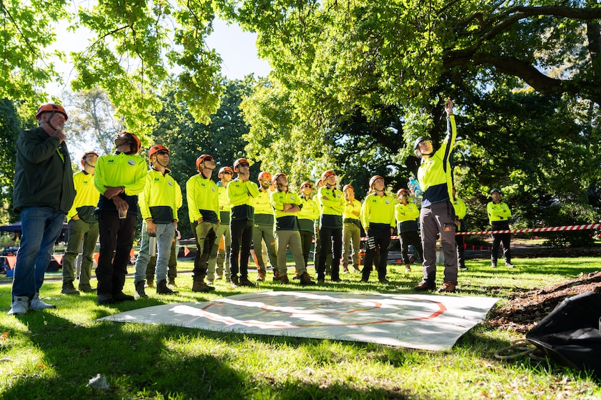 A group of about 25 people in hi-vis stand in a line in a park