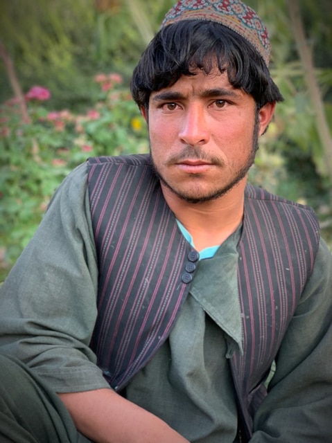 A young Afghan man sits in a garden.