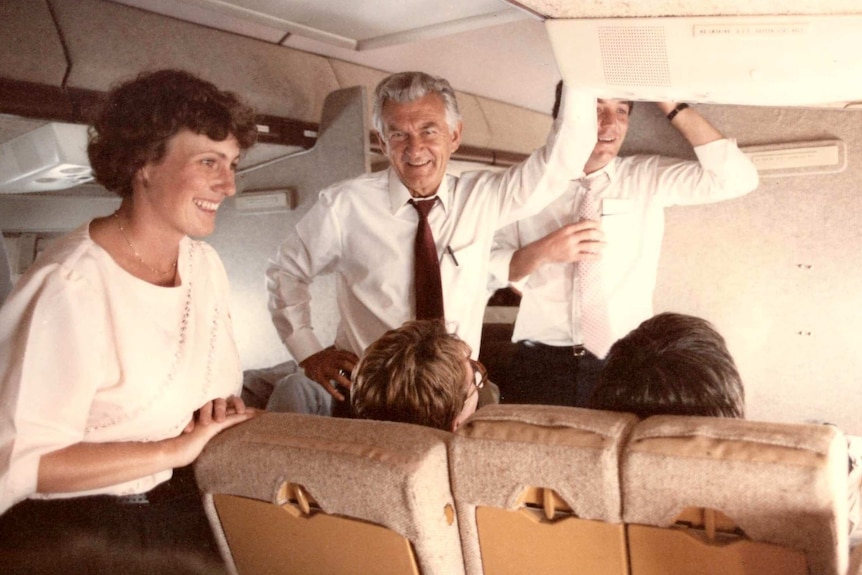 Ewart and Hawke standing in aisle of a plane.