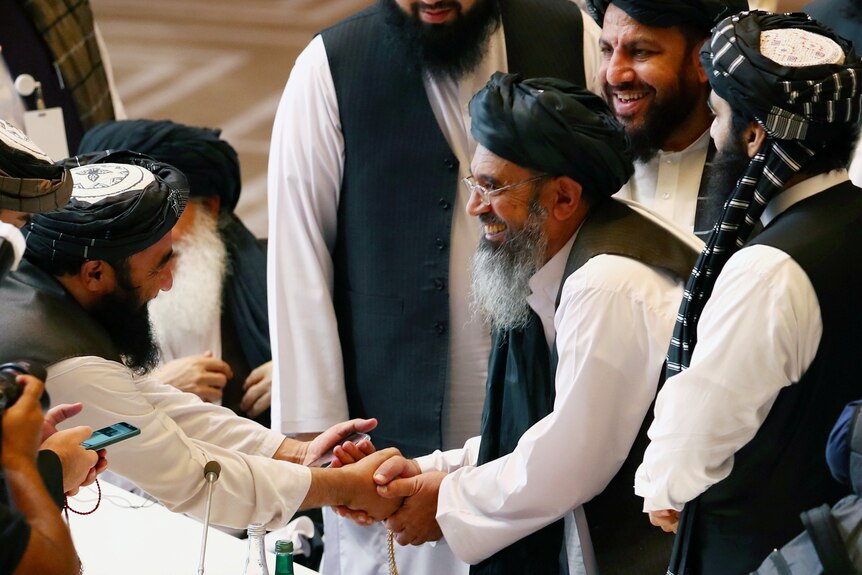 Abdul Hakim Haqqani smiles and shakes hands surrounded by other men.