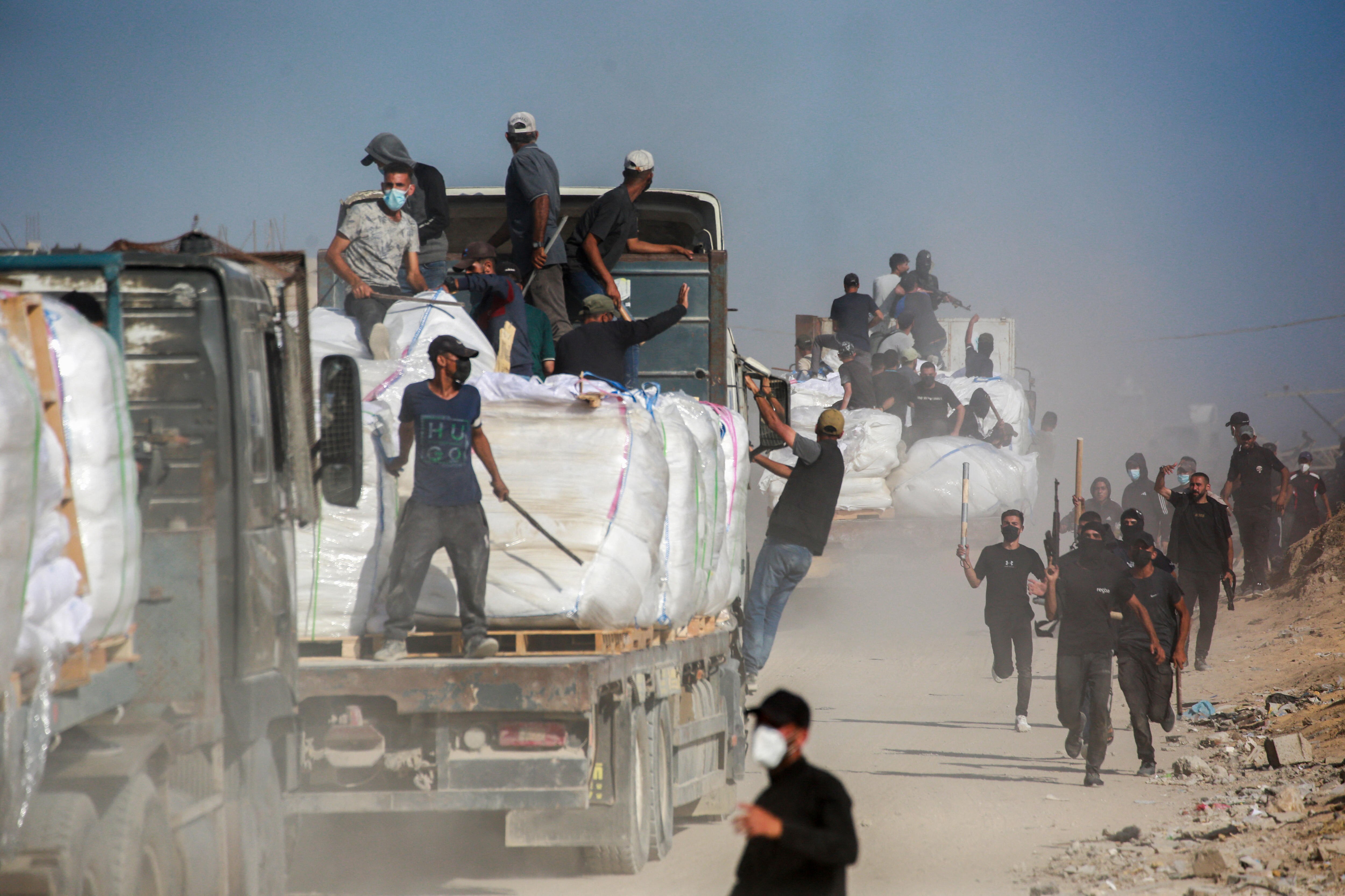 Groups of men armed with baseball bats and guns ride on and run next to trucks loaded with wrapped pallets of aid.