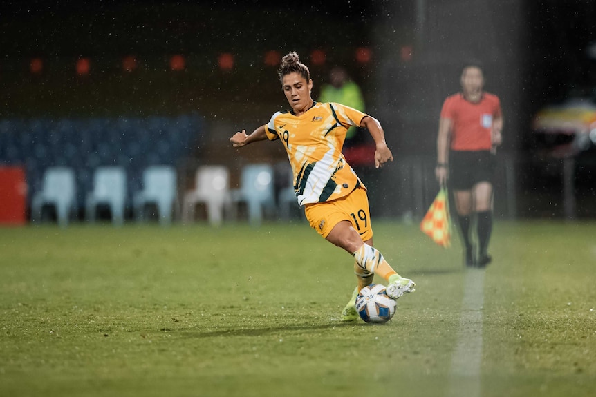 A female football player runs after the ball near the sideline.