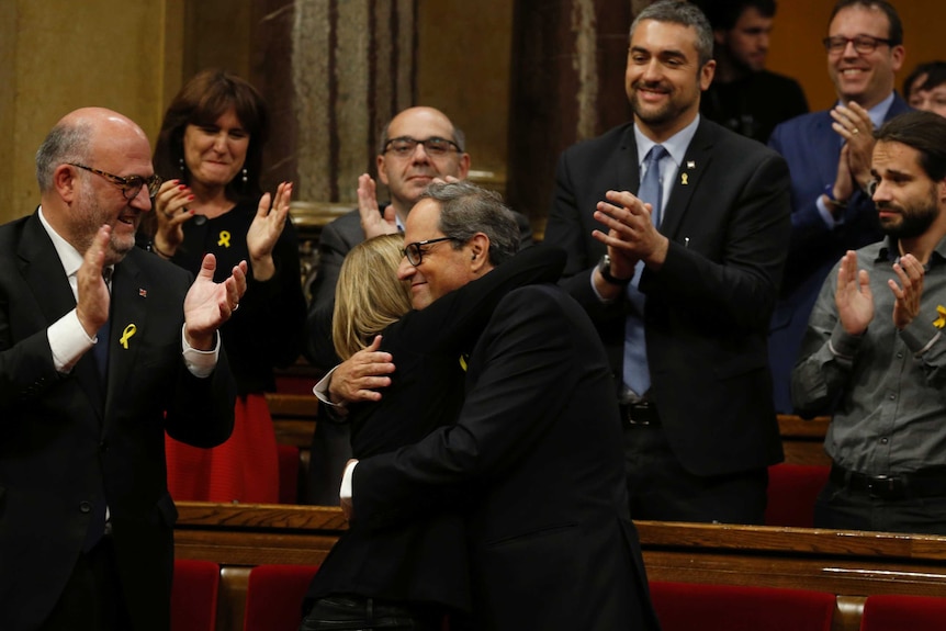 Quim Torra hugs a woman and is applauded by people around him.