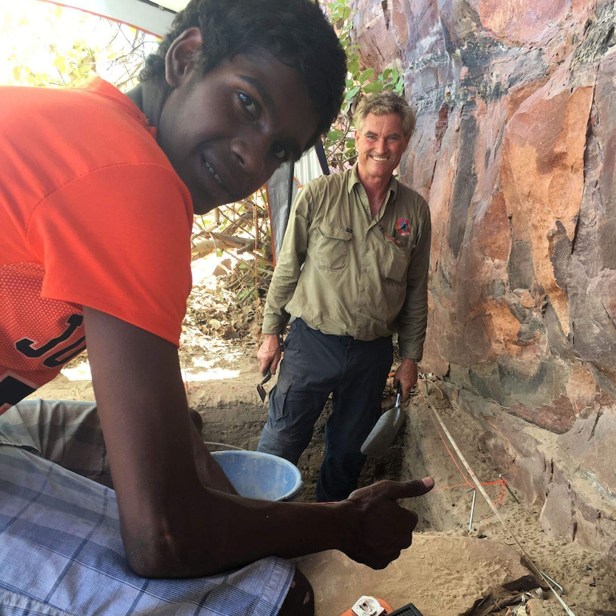 Curt Evans and Peter Veth pose for a photo standing aside an excavation pit near a rock face.