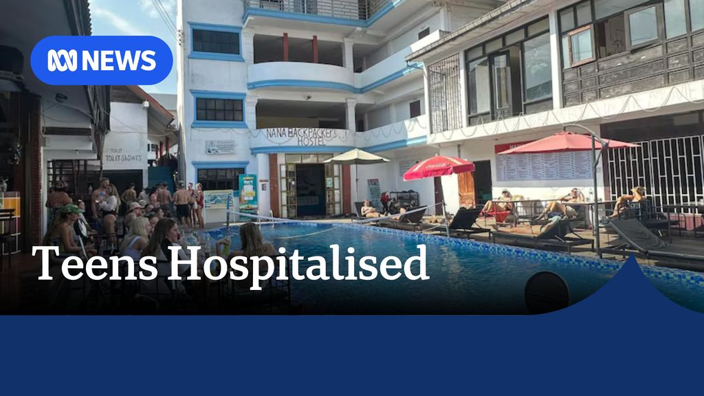 Teens Hospitalised: A pool with buildings around it featuring beach umbrellas and people lying on banana chairs.