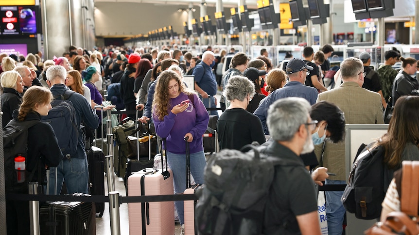 A long line of people stand with their luggage in a queue inside a terminal in London.