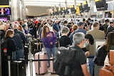 A long line of people stand with their luggage in a queue inside a terminal in London.