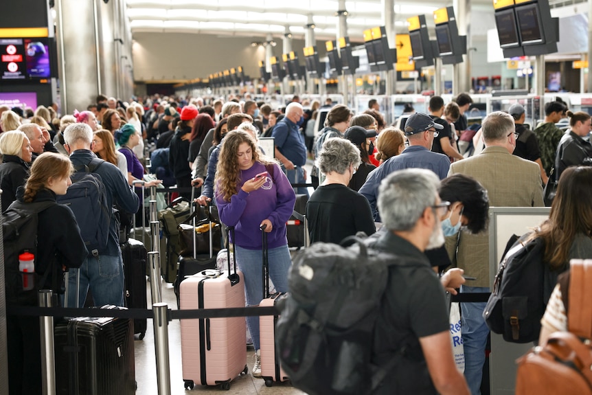 A long line of people stand with their luggage in a queue inside a terminal in London.