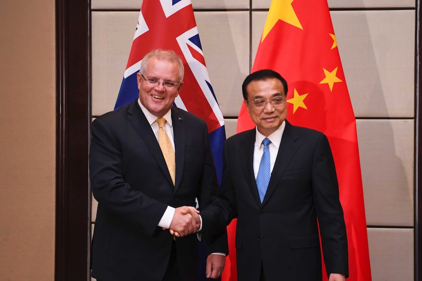 Australian Prime Minster shakes hands with the Premier of China Li Keqiang in front of their respective national flags.