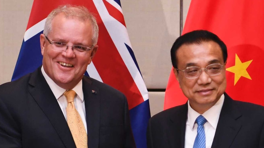 Australian Prime Minster shakes hands with the Premier of China Li Keqiang in front of their respective national flags.