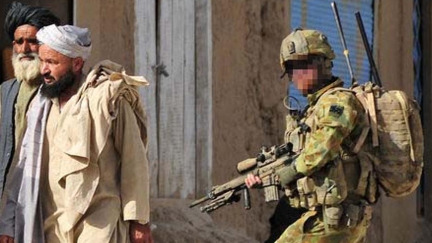A group of Afghan men walk past an Australian soldier in a village in the Chora Valley in 2010.