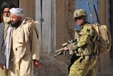 A group of Afghan men walk past an Australian soldier in a village in the Chora Valley in 2010.