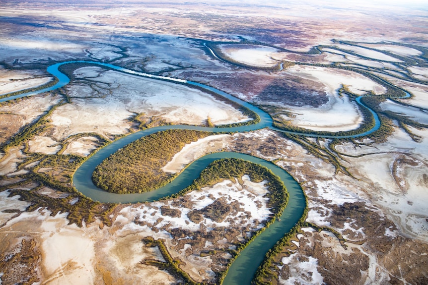 An aerial view of a blue river snaking through salt pan plains in outback Queensland