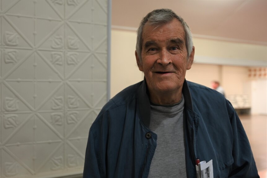 A grey-haired man wearing a jacket smiles after a meeting at Eidsvold Community Hall.