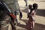 A displaced Sudanese girl, carrying a young child