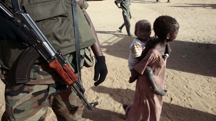 A displaced Sudanese girl, carrying a young child