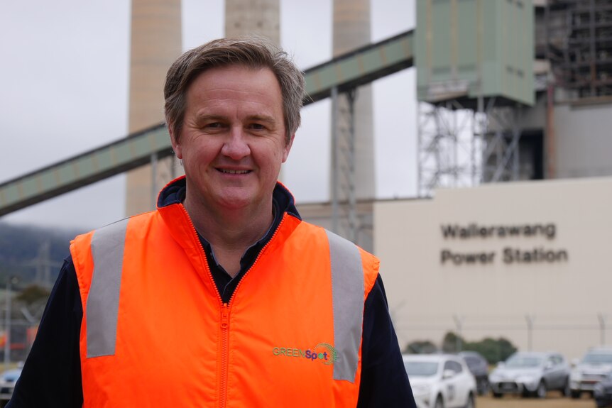 A man in a high-visibility vest stands in front of a defunct coal-fired power stations.