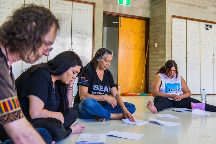 An Aboriginal woman, surrounded by Aboriginal acting students, reads from a play script