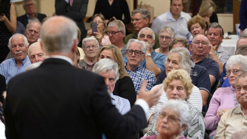 Retirees look towards the Prime Minister, who is photographed from behind speaking to the crowd