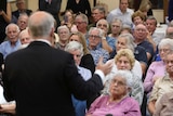Retirees look towards the Prime Minister, who is photographed from behind speaking to the crowd