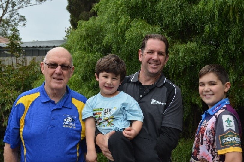 An older man standing outside with his son and two grandsons