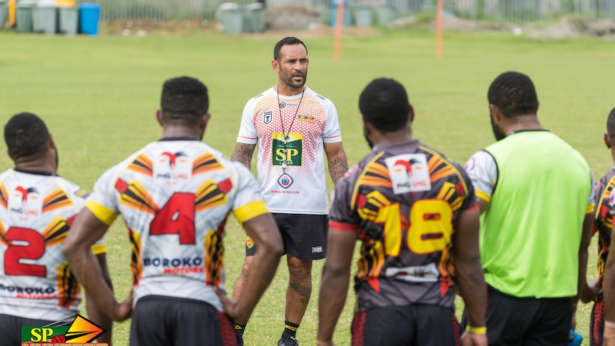 Man talks to rugby league players during training on a rugby field. 