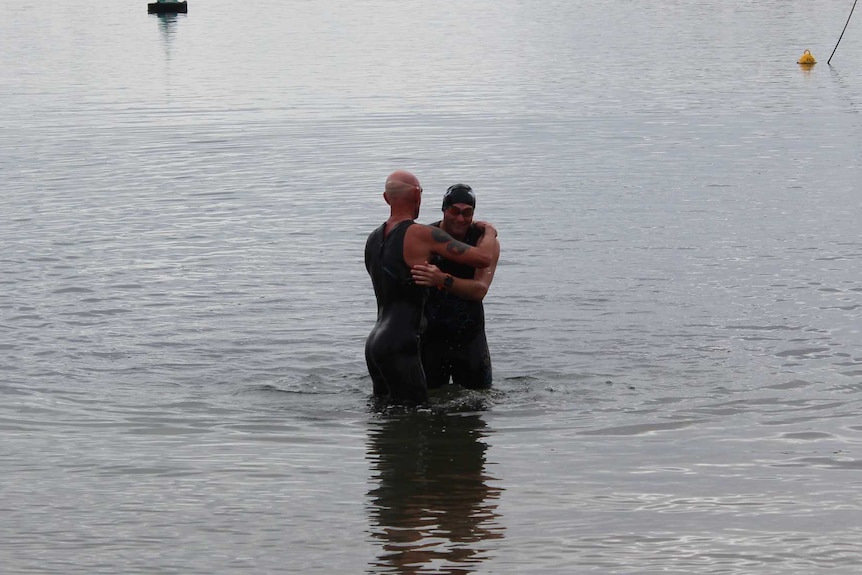 Two men in swimming gear hugging in the water.