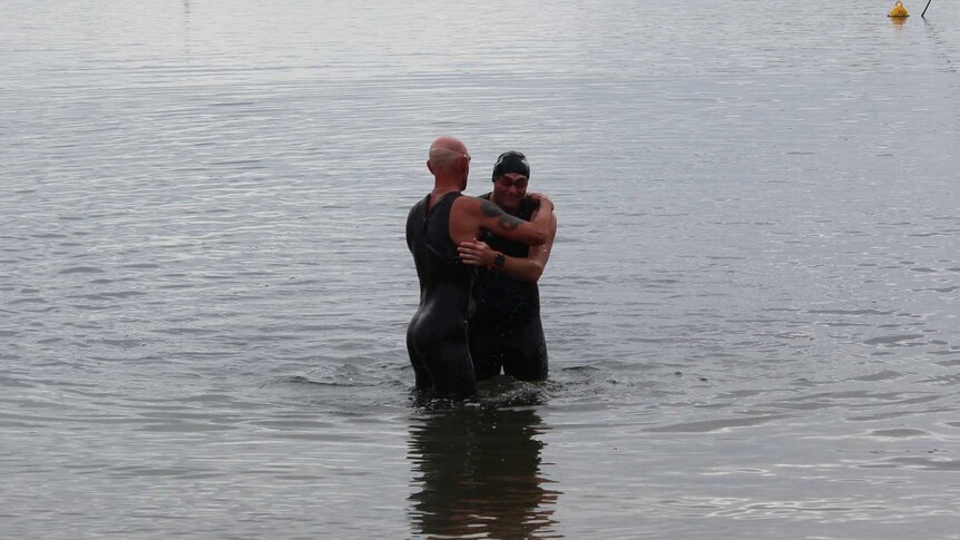 Two men in swimming gear hugging in the water.