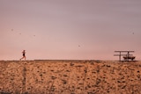 In the distance a woman runs across a dry landscape in front of a pink sky.