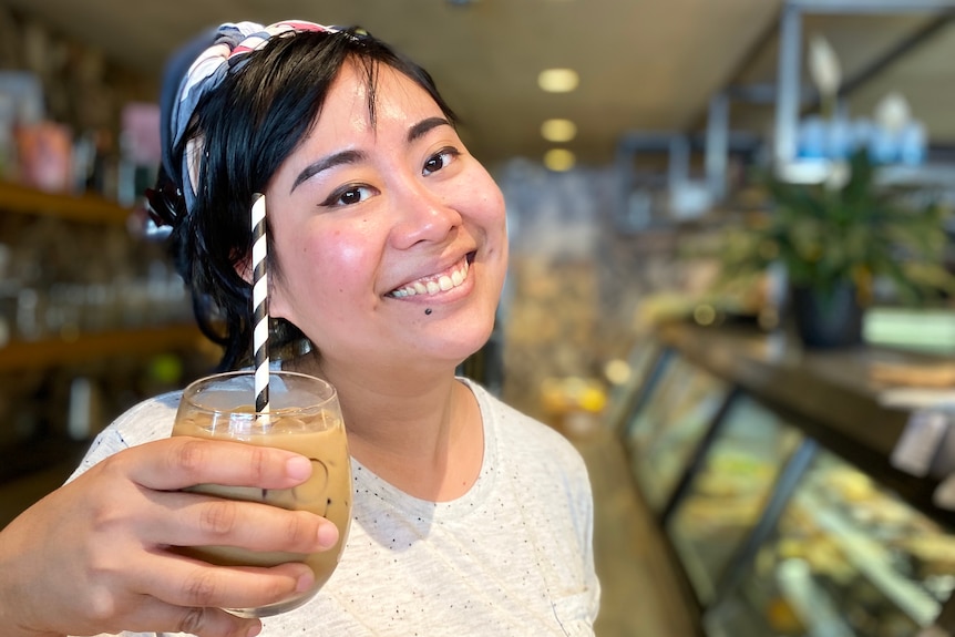 A woman holding a glass of iced coffee and smiling to camera