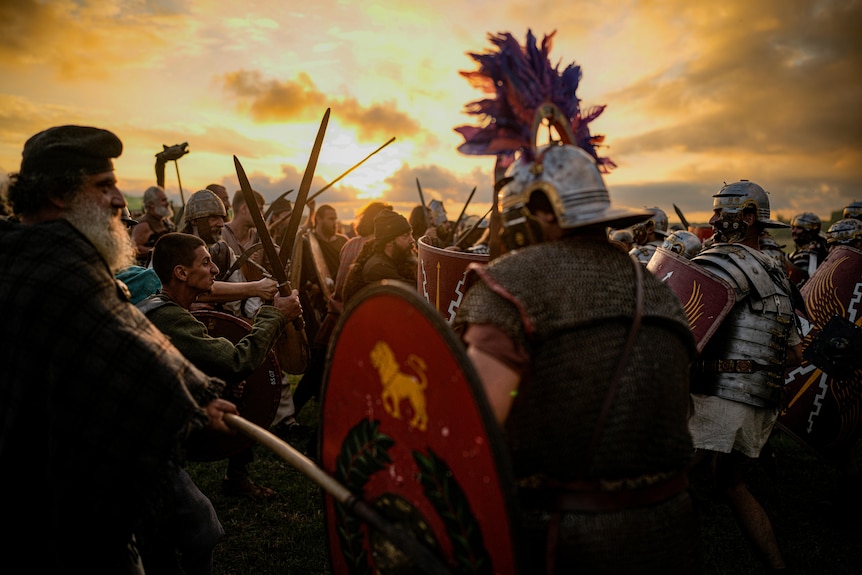 re-enactors in Roman Empire-era armour and play battle at a festival in Romania under a yellow cloudy sky