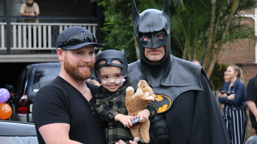 Jeff Vale holding son Eli Vale standing next to Craig Blackburn, dressed as Batman