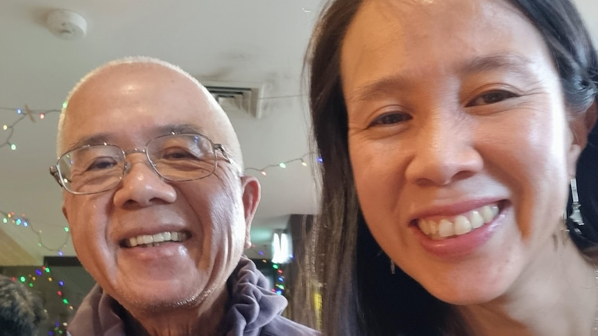 A selfie taken by a woman with black hair and earrings next to an older man in glasses and both of them are smiling.