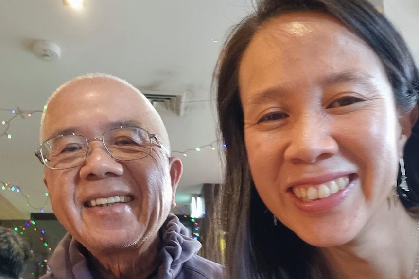 A selfie taken by a woman with black hair and earrings next to an older man in glasses and both of them are smiling.