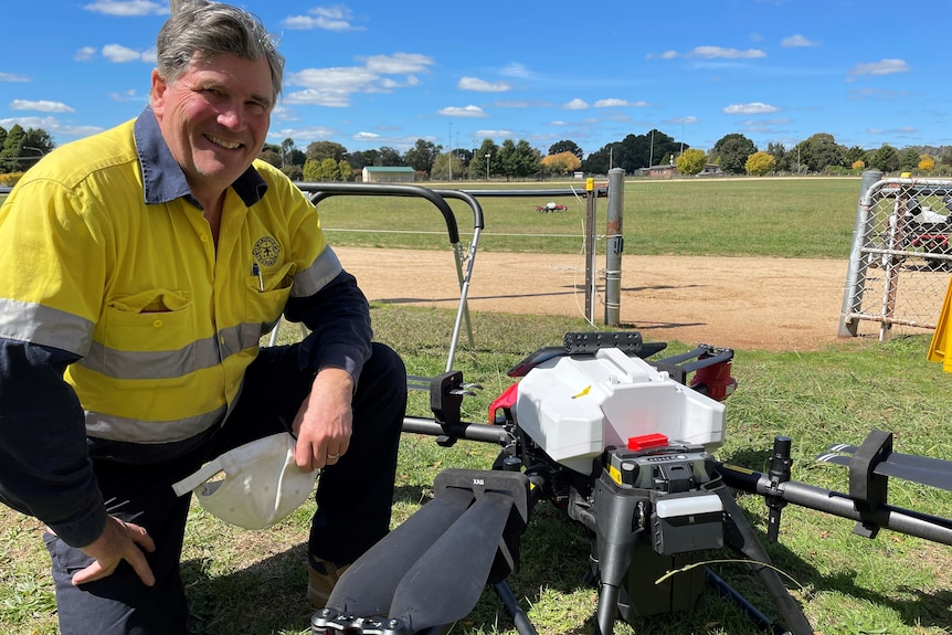 A smiling man leaning next to a drone.