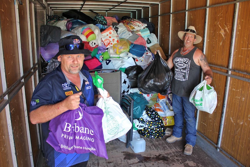 Two men are inside a truck holding aloft bags of donated goods.