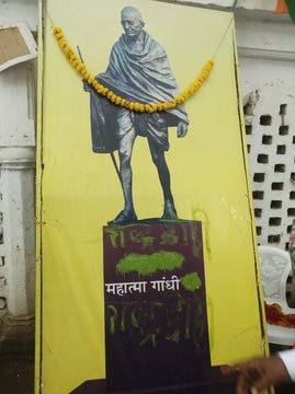 A yellow poster of Mahatma Gandhi is painted over Hindi characters in green paint.