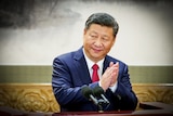 Xi Jinping in a navy suit and red tie clapping his hands and smiling slightly 